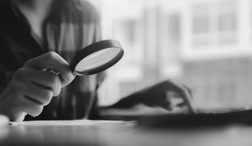 Business man using magnifying to review balance sheet annual with using laptop computer to calculating budget. audit and Check integrity before investment concept.